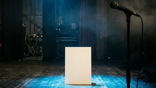 A single spotlit card on a dark stage beside a microphone silhouette